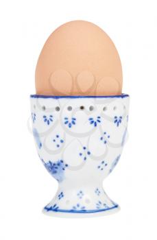 side view of brown boiled egg in ceramic egg cup with a pointy end up isolated on white background