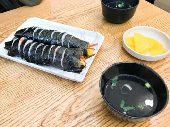 lunch with Gimbap (Korean dish made from cooked rice and other ingredients), danmuji (yellow pickled radish) and broth in local eatery in Seoul city (snapshot by mobile smartphone)