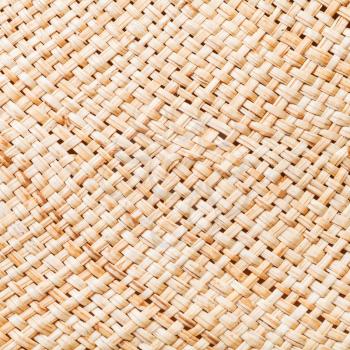 textile square background - texture of summer straw hat from interwoven raffia fibers close up