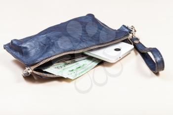 open blue leather wristlet purse bag with credit cards, smartphone and euro banknotes on pale brown table