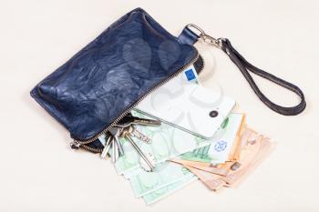top view of open pouch bag with bunch of keys, smartphone and various euro banknotes on pale brown table