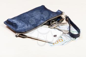 open blue leather wristlet purse bag with bunch of keys, smartphone and US dollars on pale brown table