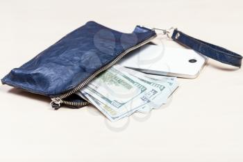 open blue leather wristlet purse bag with smartphone and US dollars on pale brown table