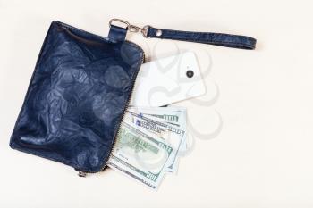 top view of open blue leather wristlet pouch bag with smartphone and US dollars on pale brown table
