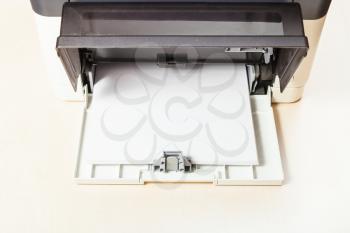 stack of white paper sheets in printer tray of multi function device on table in office