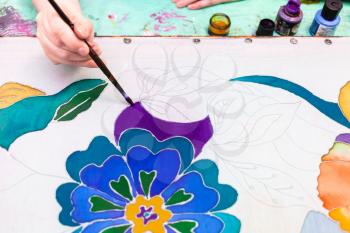 artist draws floral pattern on white silk canvas on wooden frame in cold contour batik technique