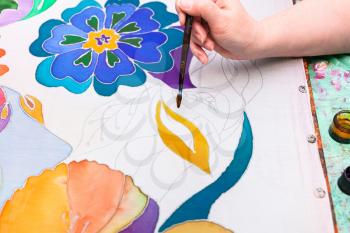 craftsman draws floral pattern on white silk canvas on wooden frame in cold contour batik technique