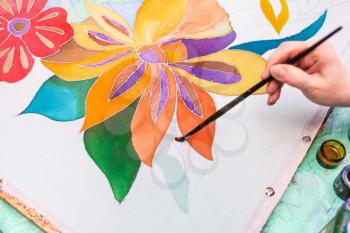 painter draws floral pattern on white silk canvas on wooden frame in cold contour batik technique