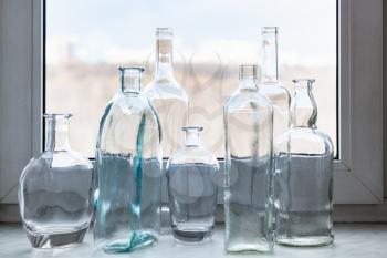 many clear bottles on windowsill and view of city park through home window on sunny spring day on background