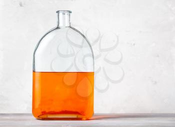 glass flask with orange watercolour solution on gray wooden board near gray concrete wall