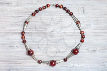 top view of handcrafted necklace from brown agate balls, ox's eye beads and silver inserts on gray wooden table close up