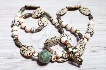 tangled handcrafted necklace from aplite cabochons, glass beads, green serpentinite ball, cracked cacholong beads and brass inserts on gray wooden table close up