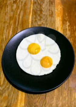 two fried eggs on black plate on wooden table in home kitchen