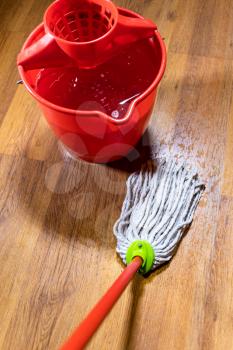 point of view of rope mop washes wooden laminate floor near bucket with water at home