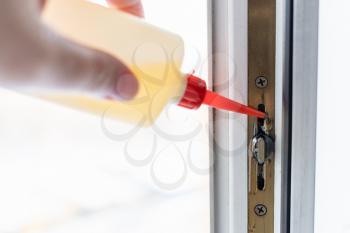hand lubricates window frame mechanism with oil from oiler close up