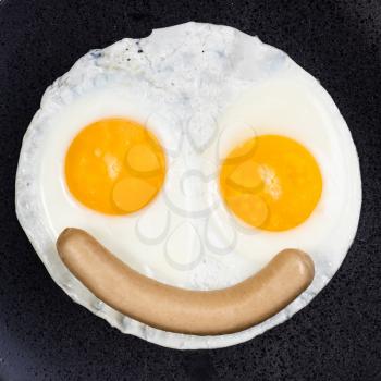 top view of fried eggs and boiled sausage on black plate close up. Fried eggs like smiling face