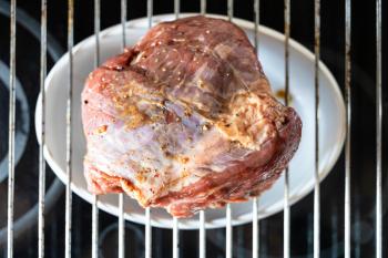 cooking Roast beef at home - marinated piece of beef on grill grate at home kitchen