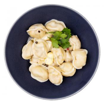 top view of boiled Pelmeni (russian dumplings filled with minced meat) with butter and decorated with green parsley leaves in black bowl isolated on white background
