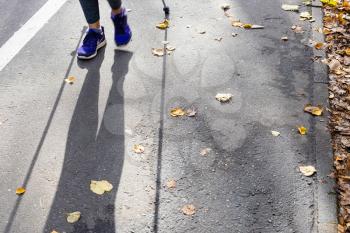 legs and shadow of walker of Nordic walking on pathway in city park on sunny autumn day