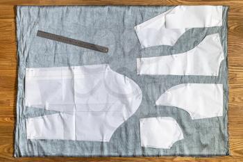 top view of paper layouts of sewing patterns of dress and steel ruler on gray fabric on wooden table at home