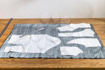 paper layouts of sewing patterns of dress on gray fabric and steel rulers on wooden table at home