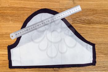 top view of one paper layout of sewing pattern of dress and steel ruler on purple fabric on wooden table at home