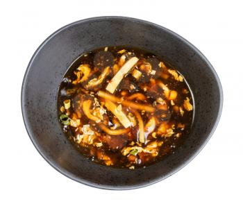 Chinese cuisine - top view of sour and hot spicy soup with shrimp and chicken (broth with chicken, shrimp, tofu, bamboo, mushrooms, egg and dark soy sauce) in black bowl isolated on white background