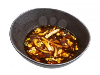 Chinese cuisine - sour and hot spicy soup with shrimp and chicken (broth with chicken, shrimp, tofu, bamboo, mushrooms, egg and dark soy sauce) in black bowl isolated on white background