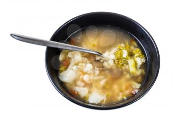 soup with stelline (italian pasta) and vegetables (cauliflower, broccoli, etc) in black bowl with spoon isolated on white background