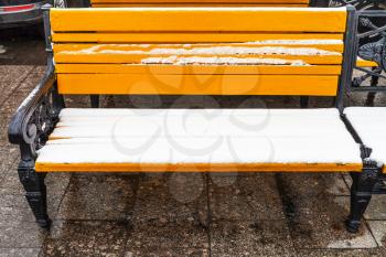 front view of yellow wooden bench covered by snow on Manezhnaya square in Moscow city in winter
