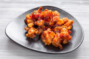 Korean Chinese cuisine - Kkanpunggi spicy fried Chicken pieces with vegetables in sweet and sour sauce on black plate close up