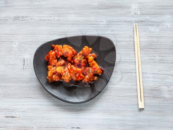 Korean Chinese cuisine - top view of Kkanpunggi spicy fried Chicken pieces with vegetables in sweet and sour sauce on black plate with chopsticks on gray table