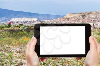 travel concept - tourist photographs of mountain flowering meadow in Goreme National Park in Cappadocia in Turkey in spring on smartphone with cutout screen with blank place for advertising