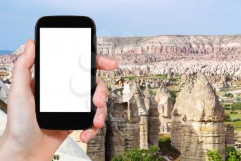 travel concept - tourist photographs of fairy chimney rocks in mountain valley of Goreme National Park in Cappadocia in Turkey on smartphone with empty cutout screen with blank place for advertising