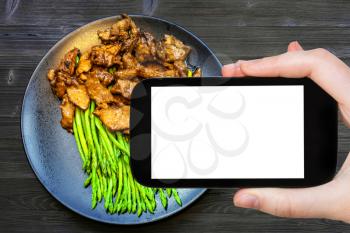 travel concept - tourist photographs of Chinese cuisine dish of Beef fried in soy sauce with green asparagus on smartphone with empty cutout screen with blank place for advertising