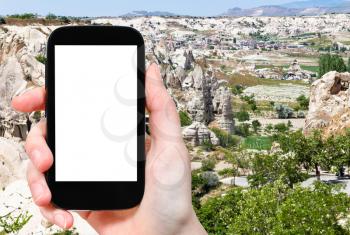 travel concept - tourist photographs of valley with fairy chimney rocks and Goreme town in Cappadocia in spring in Turkey on smartphone with empty cutout screen with blank place for advertising