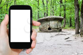 travel concept - tourist photographs of large Shapsugsky Dolmen in Abinsk Foothills of Caucasus Mountains in Kuban region of Russia on smartphone with cut out screen with blank place for advertising