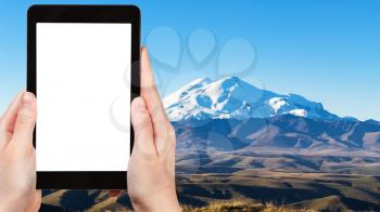 travel concept - tourist photographs of Mount Elbrus from Bermamyt Plateau at autumn morning in North Caucasus mountains of Russia on smartphone with cut out screen with blank place for advertising