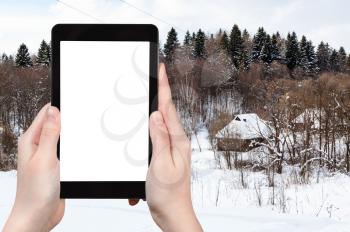travel concept - tourist photographs of russian village near forest in cloudy winter day in Smolensk region of Russia on smartphone with cut out screen with blank place for advertising