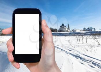 travel concept - tourist photographs of frozen river and Suzdal Kremlin with Chathedral and palace in Suzdal town in winter of Russia on smartphone with cutout screen with blank place for advertising