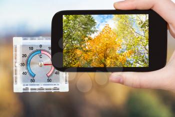 travel concept - tourist photographs yellow trees and outdoor thermometer on home window in hot autumn day on smartphone in Moscow, Russia