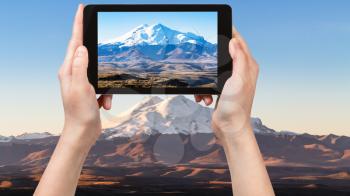 travel concept - tourist photographs of Mount Elbrus from Bermamyt Plateau in North Caucasus region of Russia at september sunrise on smartphone