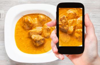 travel concept - visitor photographs of Indian cuisine of Murg Makhan Masala barbequed chicken pieces in spicy tomato and creamy curry sauce on smartphone