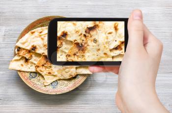 travel concept - visitor photographs of Indian cuisine of Naan flat bread baked in tandoor on brass plate on smartphone