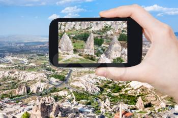 travel concept - tourist photographs of ancient houses in fairy chimney rocks in Goreme National Park in Cappadocia on smartphone in Turkey in spring