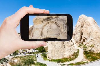 travel concept - tourist photographs of outdoor decor of ancient cave church near Goreme town in Cappadocia region on smartphone in Turkey in spring