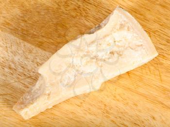 top view of piece of local italian Parmigiano Reggiano (Parmesan) hard cheese on light wooden cutting board