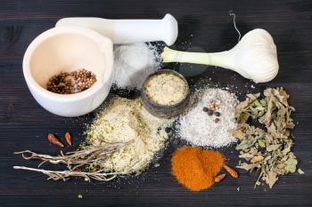 various Seasoned Salts with ingredients and mortar on dark brown wooden board