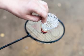 hand holds shuttlecock over badminton racquet on outdoor earth ground