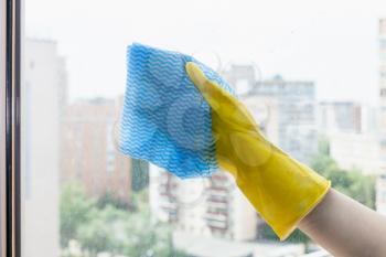 hand wipes glass of home window in urban apartment house by blue rag